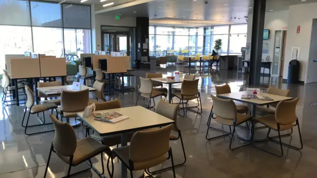 A modern, brightly lit space with beige chairs and square tables on a shiny floor. Large windows and an open layout create an inviting, airy space.