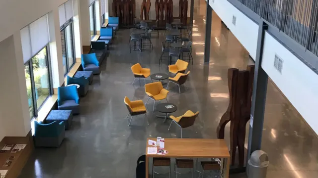 Spacious lobby with yellow and blue seating, wooden sculptures, and large windows. A polished floor reflects natural light creating a welcoming atmosphere.