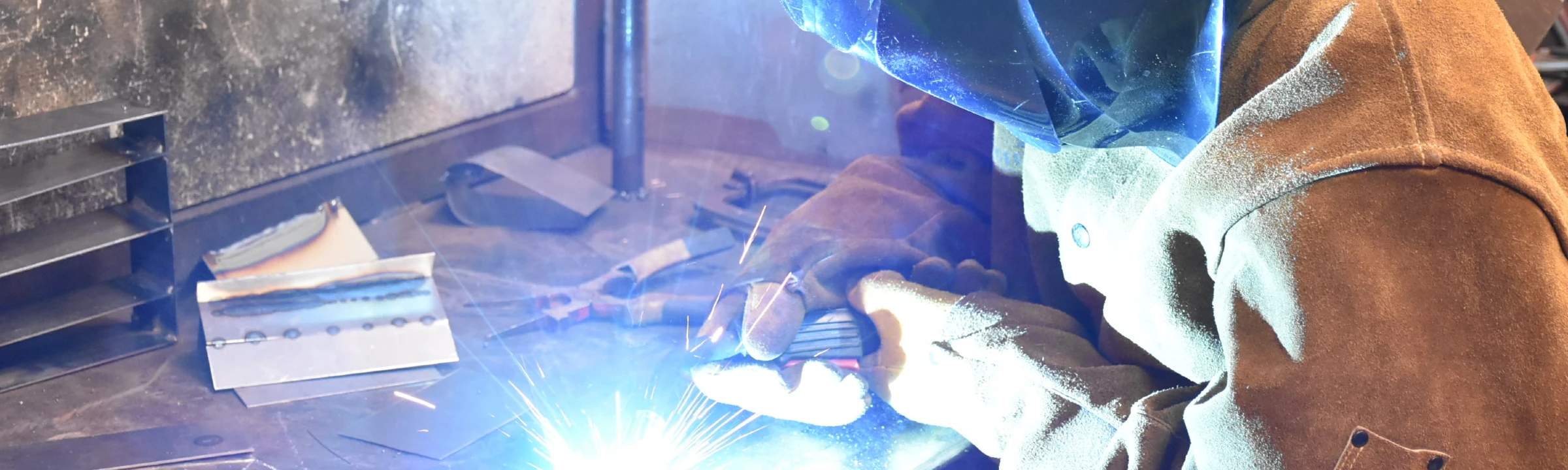 Sparks fly as welding student wearing protective equipment and gloves works on a project