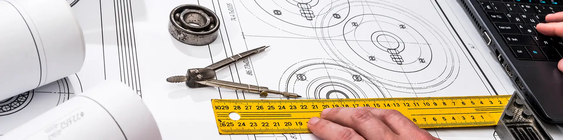 Person measuring a blueprint with a ruler and using a computer