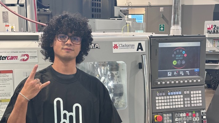 Participant in the Metallica Scholars initiative poses in front of CNC machine doing 