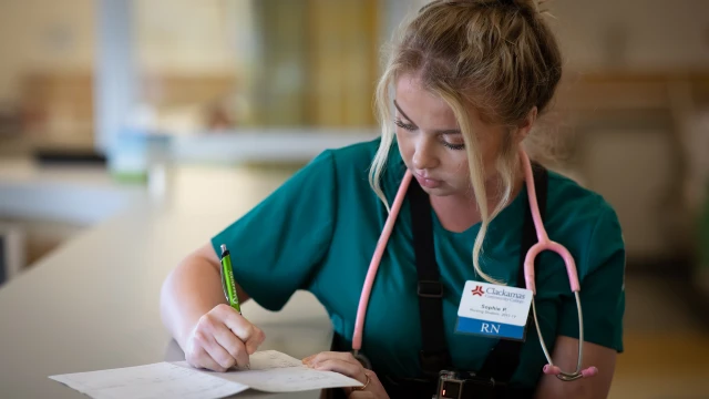Nursing student wearing scrubs and a stethoscope fills out paperwork
