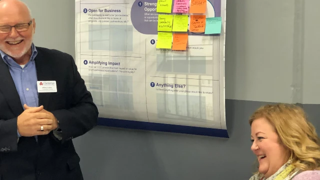 Two participants in business summit on the Wilsonville campus with a chart with sticky notes behind them on the wall