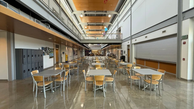 Spacious, well-lit open space with wooden chairs and square tables, glossy floors, gray lockers, and a modern industrial design featuring high ceilings.