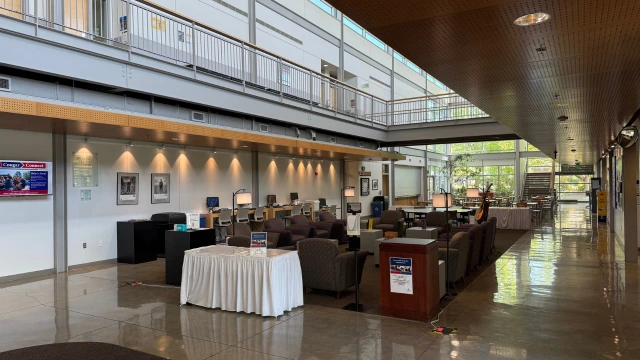 A spacious, modern room with high ceilings, abundant natural light, and a sleek design. It features comfortable seating, computers, and a quiet atmosphere.